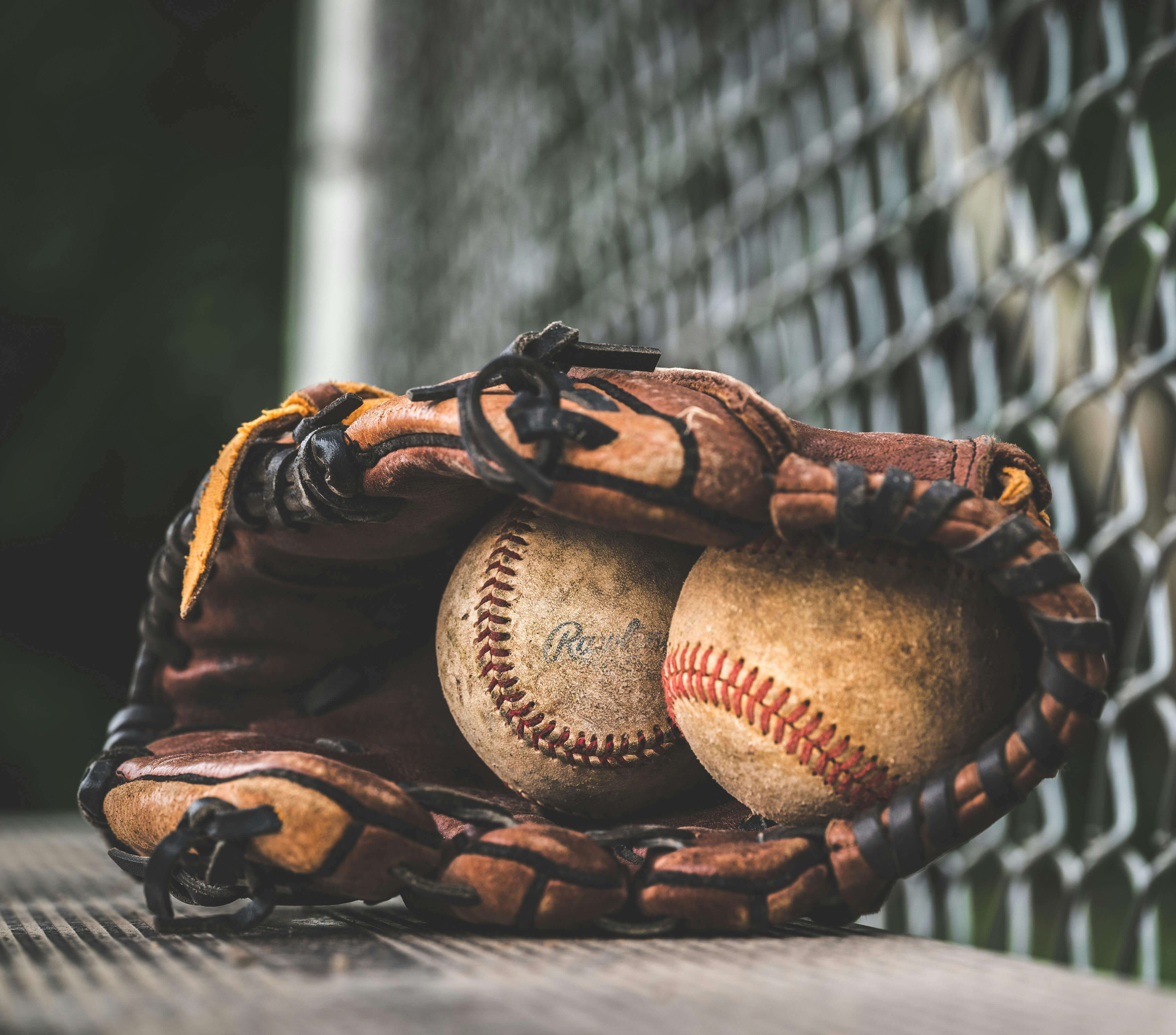 A baseball glove holding two baseballs on a dugout bench.